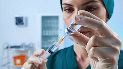 Врач в зеленом халате набирает лекарство в шприц.